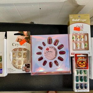 Peut inclure: Plusieurs bo&icirc;tes de faux ongles de diff&eacute;rentes couleurs et styles. Les ensembles comprennent des couleurs iris&eacute;es, &agrave; paillettes et unies. Certaines bo&icirc;tes portent les noms de marque "Kiss", "Crystal", "GoldFinger" et "Impress".