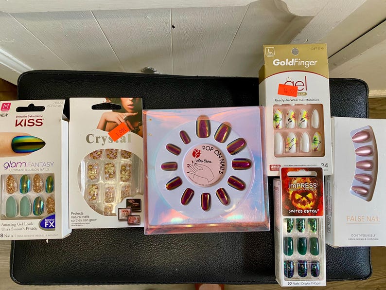 Peut inclure: Plusieurs bo&icirc;tes de faux ongles de diff&eacute;rentes couleurs et styles. Les ensembles comprennent des couleurs iris&eacute;es, &agrave; paillettes et unies. Certaines bo&icirc;tes portent les noms de marque "Kiss", "Crystal", "GoldFinger" et "Impress".