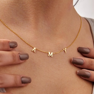 May include: A delicate gold necklace featuring the letters A, M, and Y. The pendant letters are suspended from a fine gold chain. The necklace is a personalized jewelry item.