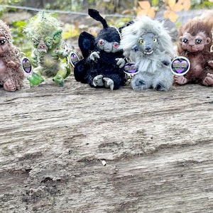 Op de afbeelding: Vijf fantasie-wezen beeldjes met gedetailleerde kenmerken, waaronder vacht, klauwen en expressieve gezichten. De wezens zijn in verschillende kleuren, zoals bruin, groen en zwart, en zijn geplaatst op een verweerd houten oppervlak. Elke figuur heeft een label.