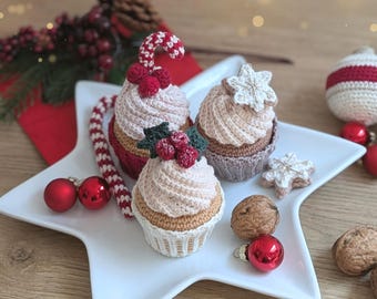 May include: Three crocheted cupcakes on a white star-shaped plate. One cupcake features a red and white candy cane and red berries, another has a white snowflake, and the third has green holly leaves with red berries. Includes walnuts and red ornaments.