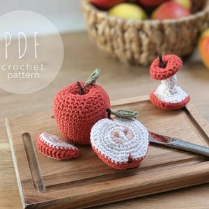 Puede incluir: Patrón de ganchillo de manzana con una manzana entera, media manzana y una rodaja. Las manzanas son rojas con hojas verdes y detalles blancos y rosas. El texto "PDF crochet pattern" es visible.