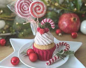 May include: A crocheted cupcake with a dark red base, tan middle, and white frosting topped with red berries and a small candy cane. Two crocheted lollipops in red and white swirls are attached to sticks, one wrapped in clear plastic.