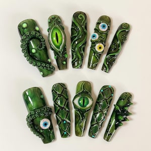 May include: A set of ten green press-on nails with a glossy finish. The nails feature various designs, including tentacles, stylized eyes, and textured patterns. The color palette includes shades of green, white, and blue.