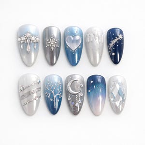 May include: A set of ten artificial nails with winter-themed designs. The nails feature various shades of blue, silver, and white, with embellishments like snowflakes, hearts, and celestial patterns. Some nails have glitter accents and crystal details.
