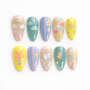 May include: A collection of ten artificial nails with various designs. The designs include rainbows, clouds, flowers, bows, stripes, hearts, and a rocket ship. The nails are painted in pastel colors, including pink, blue, yellow, and green, with glitter accents.