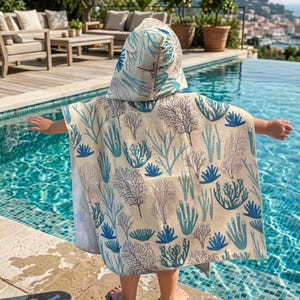 May include: A hooded beach towel with a sea-themed pattern in shades of blue and gray. The towel is beige and features a design of coral and seaweed. The child is standing near a pool.