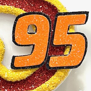 May include: Orange and black glitter number 95. The numbers are outlined in black and have a sparkly orange finish.