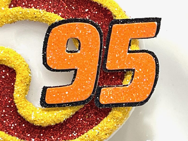 May include: Orange and black glitter number 95. The numbers are outlined in black and have a sparkly orange finish.