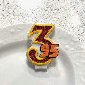 May include: A red and gold glitter birthday candle with the number 3 and 95 on it.
