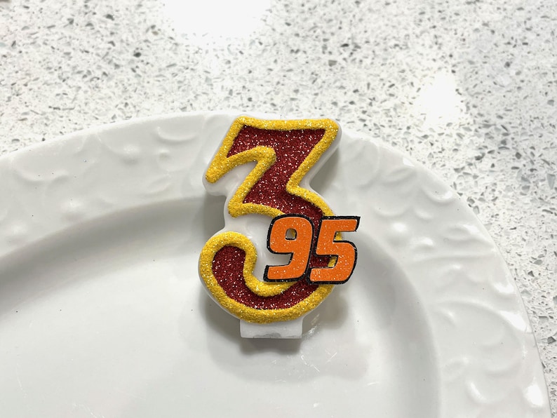 May include: A red and gold glitter birthday candle with the number 3 and 95 on it.