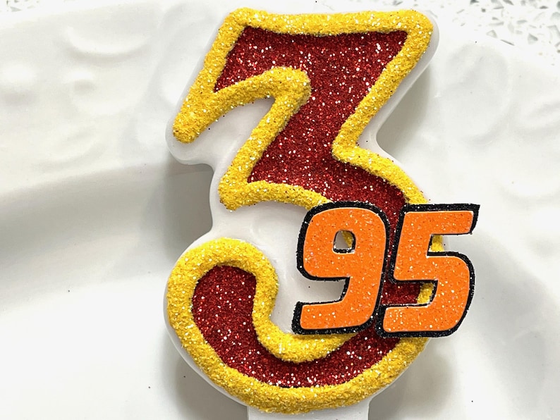 May include: Red and yellow glittery birthday candle shaped like the number 95. The number 95 is in orange with a black outline.