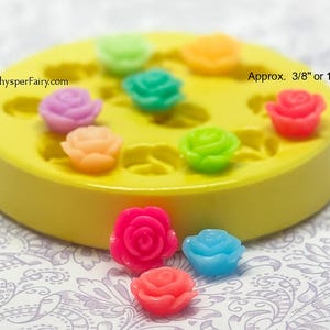 May include: A collection of colorful, miniature rose-shaped embellishments. The roses are in shades of pink, orange, green, blue, and purple. They are approximately 3/8 inch in size. A yellow mold with rose-shaped cavities is also present.