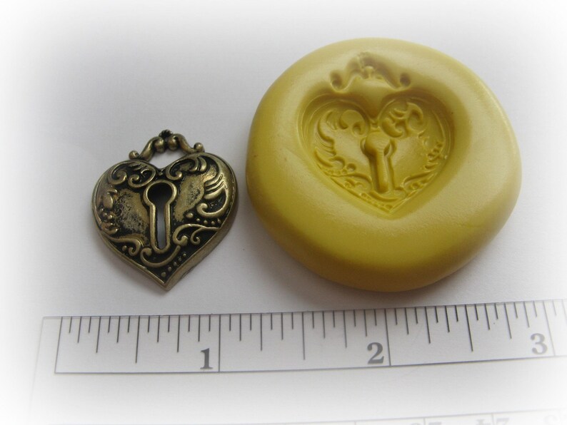 May include: A heart-shaped antique brass lock and a yellow silicone mold. The lock features a keyhole and ornate detailing. The mold has a heart-shaped impression with a keyhole design. The lock measures approximately 1 inch in width.