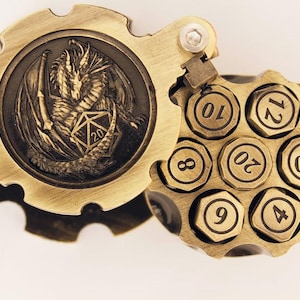 May include: A brass-colored, steampunk-style dice holder. The top features a dragon and a D20 die. The cylinder holds seven dice, each with a number. The design is detailed and intricate, with a vintage aesthetic.