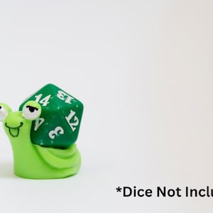 Puede incluir: Una caprichosa figura de caracol verde lima con un dado verde de 20 caras en su espalda. El dado tiene números blancos. El caracol tiene ojos saltones y una cara sonriente. El texto "*Dice Not Included" está en la parte inferior.