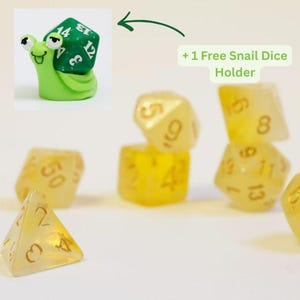 May include: A collection of yellow polyhedral dice with gold numbering, including a four-sided die, and a green snail dice holder with a green and white die. The text reads "+ 1 Free Snail Dice Holder".