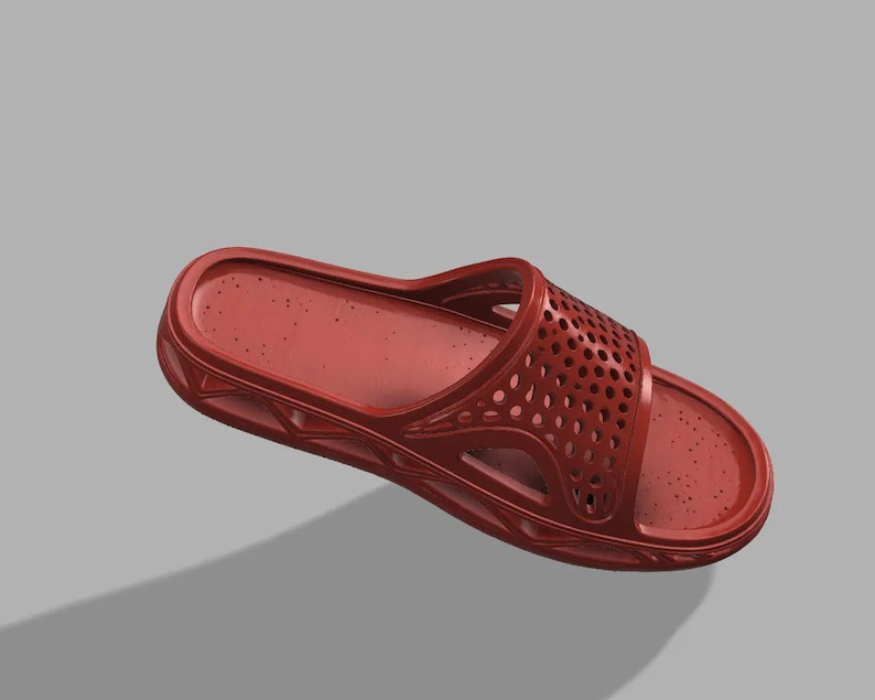 May include: A single red slide sandal with a perforated strap. The sandal is made of a solid material and has a contoured footbed. The design includes a series of small holes on the top strap for ventilation. The sandal is shown against a grey background.