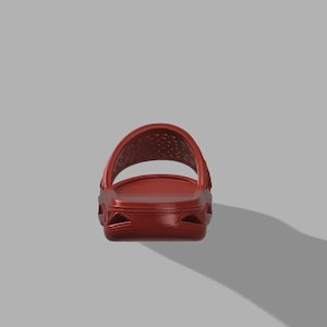 May include: A single red slide sandal, seen from the front. The sandal features a moulded design with a strap across the top and a textured footbed. The colour is a deep, solid red.