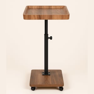 May include: A wooden, adjustable side table with a square top and base. The tabletop has a raised edge. The black metal support column has a height adjustment knob. The base has four small wheels for easy movement.