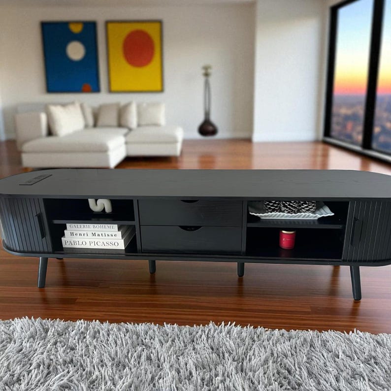 May include: A black, low-profile entertainment center with a rounded shape. It features two drawers, open shelving, and cabinet doors. The unit is set on angled legs and has a textured front. Books and decorative items are visible inside.