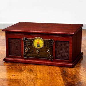 May include: A vintage-style wooden stereo system with a rich, dark red finish. The front panel features a brass-colored control panel with a yellow dial and digital display. Speakers are located on either side of the control panel.