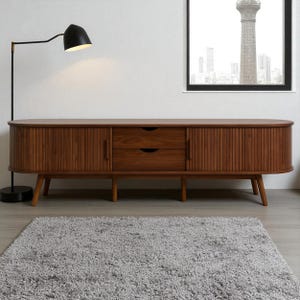 May include: A mid-century modern style wooden media console with two drawers and two doors. The doors have vertical grooved detailing. The console is supported by angled wooden legs. A black floor lamp with a curved arm and a black lampshade is to the left.