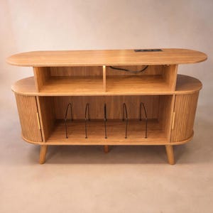 May include: A light-colored wooden record player console with an oval top and rounded sides. It features open shelving, a cabinet with a door, and metal dividers for record storage. The console has four tapered legs.