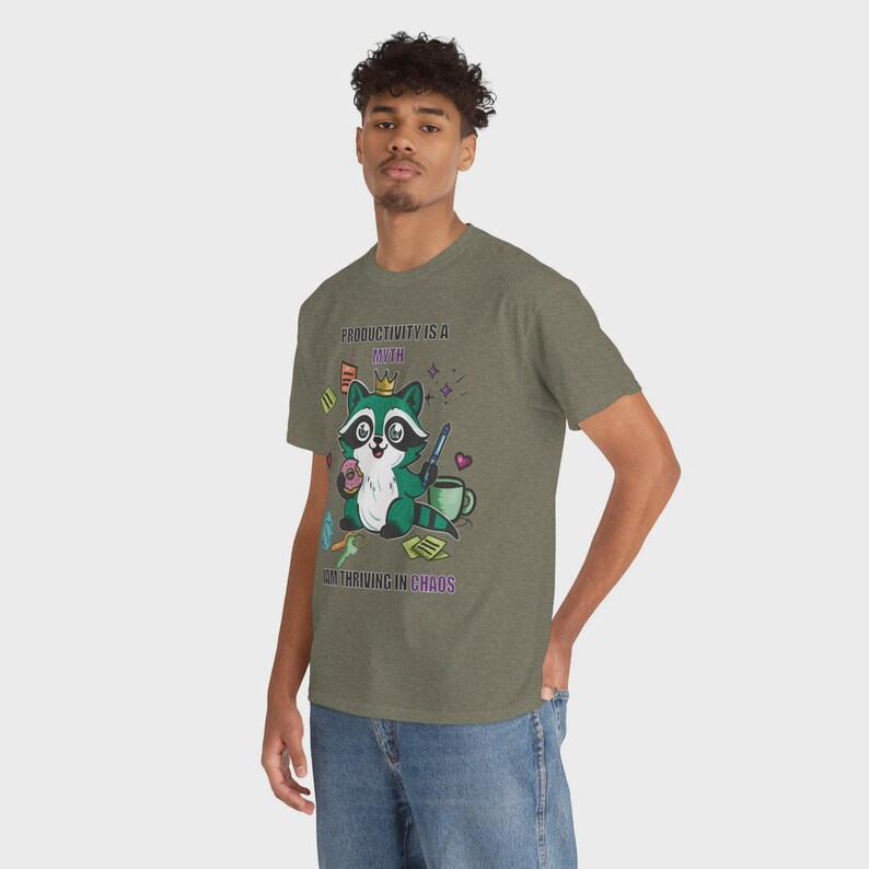 May include: Olive green t-shirt featuring a cartoon raccoon wearing a crown and holding a donut. The text on the shirt reads "PRODUCTIVITY IS A MYTH, I'M THRIVING IN CHAOS."