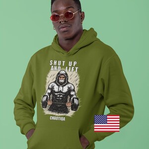 May include: Olive green hoodie with a graphic of a weightlifter and the text "SHUT UP AND LIFT" and "CHAOITQA". The hoodie has a front pocket and a US flag patch.