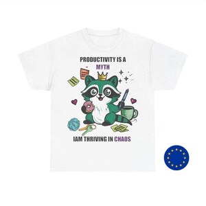 May include: White t-shirt featuring a cartoon raccoon wearing a crown, holding a pen and donut, with the text "PRODUCTIVITY IS A MYTH" and "IAM THRIVING IN CHAOS". The raccoon is surrounded by office supplies.