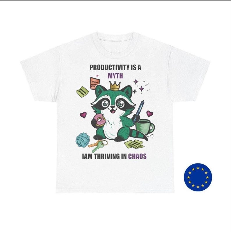 May include: White t-shirt featuring a cartoon raccoon wearing a crown, holding a pen and donut, with the text "PRODUCTIVITY IS A MYTH" and "IAM THRIVING IN CHAOS". The raccoon is surrounded by office supplies.