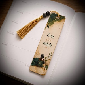 Könnte beinhalten: Ein rechteckiges Lesezeichen mit cremefarbenem Hintergrund, grünen Aquarellakzenten, botanischen Illustrationen und einer kleinen braunen Flasche mit ätherischem Öl. Der Text lautet Zeit für mich. Es hat eine goldene Quaste und zwei schwarze Lavaperlen.