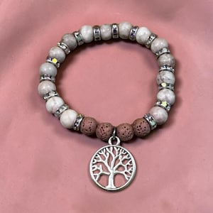 Può includere: Un braccialetto elastico con perline rotonde in pietra marmorizzata bianca e grigia alternate a distanziatori color argento incastonati con piccoli cristalli trasparenti. Quattro perline di lava marrone porose centrano un ciondolo ad albero.