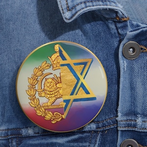 May include: A round pin with a gold border featuring a design that combines a Star of David with a lion and crown emblem. The pin has a rainbow gradient background and is set against a denim jacket.