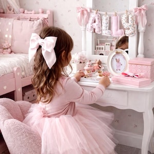 May include: A white vanity table with a mirror featuring a hanging banner that spells out the name ALLY in fabric letters. The vanity is decorated with a small oval framed picture, a pink box, and various small trinkets on the tabletop surface.