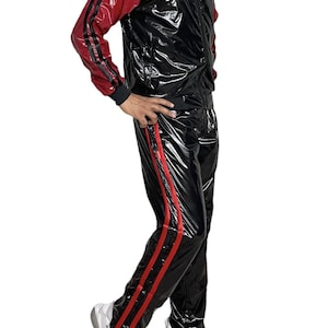 Puede incluir: Chándal negro y rojo. La chaqueta tiene mangas rojas y cuerpo negro con cuello alto. Los pantalones tienen rayas rojas en los laterales. El traje es de material brillante. Zapatillas deportivas blancas completan el look.