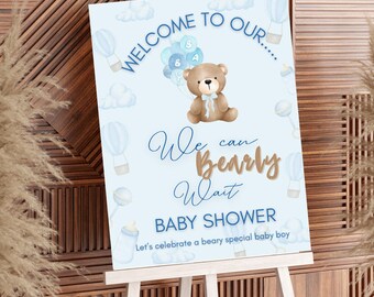 Könnte beinhalten: Hellblaues Babyparty-Schild auf einer Staffelei. Auf dem Schild steht "Welcome to Our..." und "We can Bearly Wait BABY SHOWER". Ein brauner Teddybär hält blaue Luftballons. Der Text "Let's celebrate a beary special baby boy" steht unten.