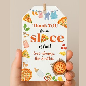 K&ouml;nnte beinhalten: Ein wei&szlig;es Geschenkanh&auml;nger mit Pizza-Motiv, gehalten von einer Hand. Das Etikett zeigt Pizzast&uuml;cke, eine ganze Pizza, Babykleidung und den Text "Thank YOU for a slice of fun!" und "love always, the Smithis".