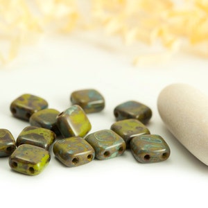 May include: A group of small, square, green and brown ceramic beads with a mottled, speckled finish. The beads have two holes each.