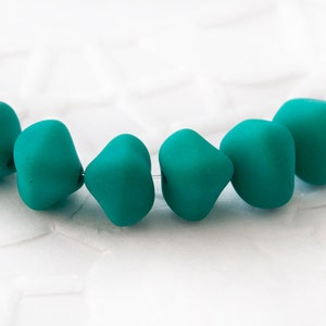 Puede incluir: Una hebra de cuentas de vidrio azul turquesa, cada cuenta está facetada y tiene una forma ligeramente irregular.