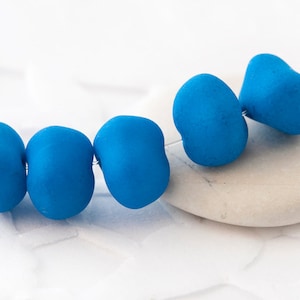 Könnte beinhalten: Eine Schnur mit fünf blauen Glasperlen, jede mit einer leicht unterschiedlichen Form. Die Perlen sind auf einem dünnen Draht aufgefädelt und in einer Reihe angeordnet.