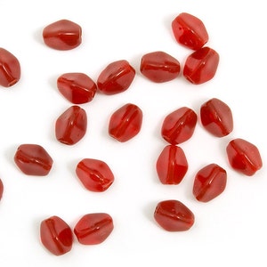 Può includere: Un gruppo di 17 perline di vetro rosso, ciascuna con una forma ovale leggermente irregolare. Le perline sono sparse su una superficie bianca.