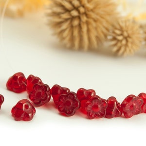 Puede incluir: Una hebra de cuentas de vidrio rojo en forma de flor. Las cuentas son pequeñas y tienen un diseño floral delicado.