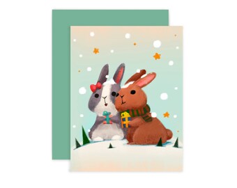 Pode incluir: Um cartão de Natal com dois coelhos em uma paisagem nevada. O coelho à esquerda é cinza com um laço vermelho e está segurando uma caixa de presente azul. O coelho à direita é marrom com uma echarpe verde e está segurando uma caixa de presente amarela. O fundo é azul claro com flocos de neve brancos.