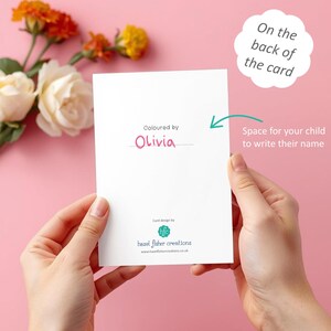 May include: A white card held by hands, with the text "Coloured by Olivia" in pink. The card also has the text "Space for your child to write their name" and "On the back of the card". Flowers are in the background.