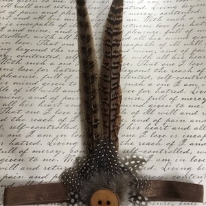 May include: Three brown and white feathers with a brown button in the center. The feathers are arranged in a fan shape and have a spotted pattern. The button has two holes.