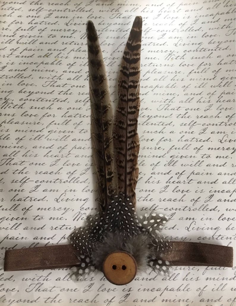 May include: Three brown and white feathers with a brown button in the center. The feathers are arranged in a fan shape and have a spotted pattern. The button has two holes.