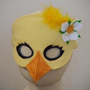 May include: A yellow felt chick mask with black eyes, an orange beak, and a white felt flower with green leaves.