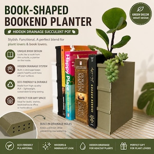 Puede incluir: Una maceta con forma de libro de color verde oliva con un sistema de drenaje oculto, colocada junto a varios libros de tapa dura. La maceta presenta un diseño rectangular con orificios de drenaje visibles en la base y una suculenta.